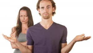 A man shrugging while his angry looking wife stands in the background