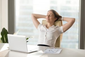 A woman reclining her chair with her hands behind her head in front of a laptop